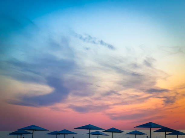 Peaceful evening scene with beach umbrellas silhouetted against a vibrant sunset sky with soft clouds.