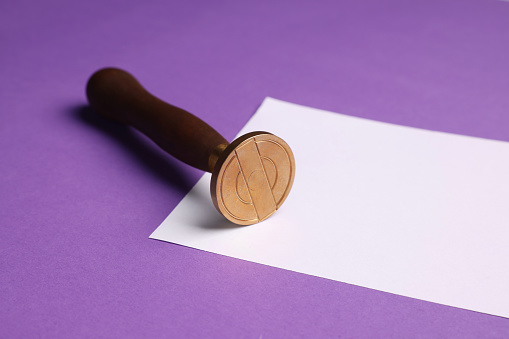 One stamp tool and sheet of paper on purple background, closeup