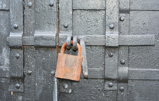 A close up on a rusty padlock on an old, antique black metal door as a symbol of mystery, privacy or secret.