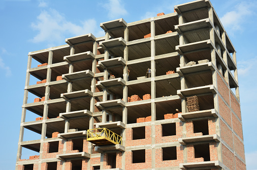 A high-rise building under construction. Building contractors on a building platform  are laying masonry vertical walls of a residential building under construction.