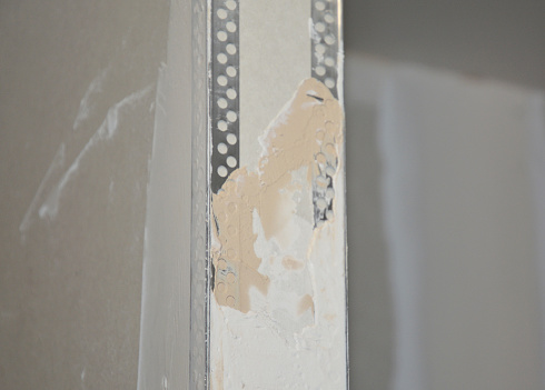 Plastering drywall corner: A close-up on plastering a drywall partition wall over installed angle beads during house renovation.