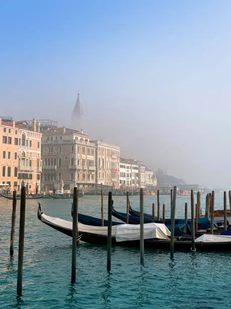 Venice Grand Canal winter morning fog partially obscuring St Mark's Campanile. Gondolas in the foreground. Copy space at top.