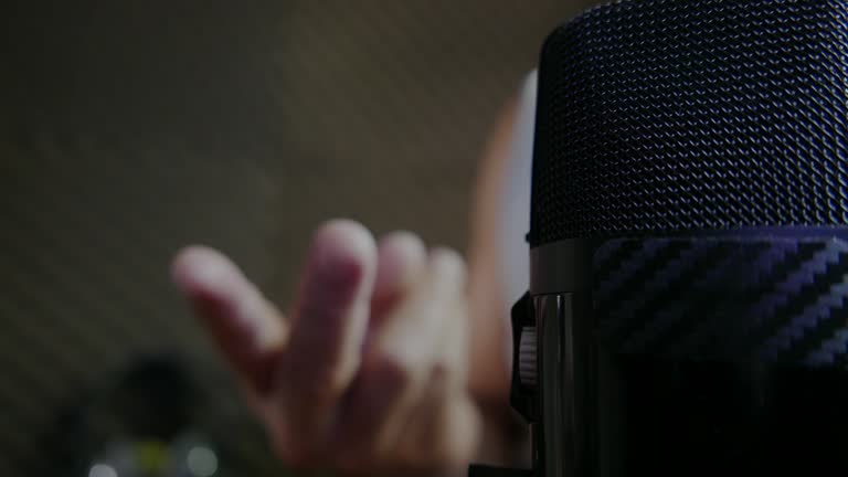 Person recording a podcast in a recording studio: close-up shot of a microphone in a podcast studio. Person speaking on a podcast. Person speaking into microphone. Podcasting. Podcast episode.  Podcast day. Person recording audio in a soundproof room