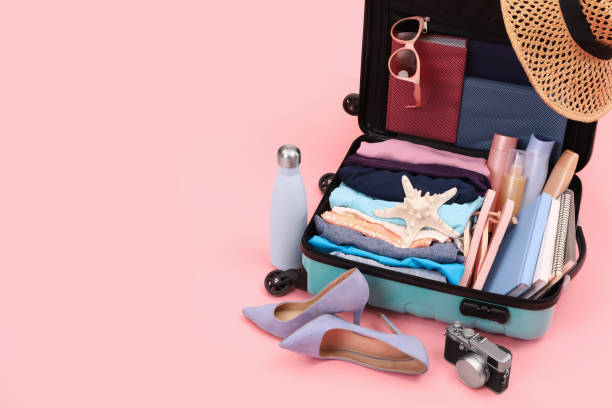 istock Open suitcase with clothes, beach accessories and shoes on pink background, space for text. Summer vacation 1954356594