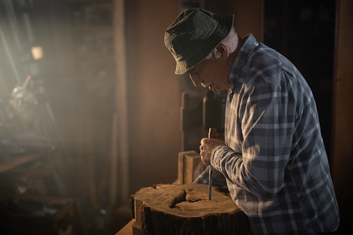One man, senior carpenter carving wood with chisel in his workshop.
