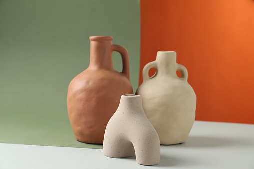 Clay flagons and vase on color background