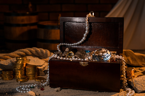 Chest with treasures, golden coins and scattered sand on table