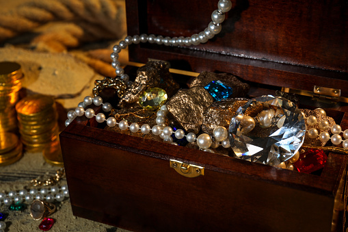 Chest with treasures, golden coins and scattered sand on floor, closeup