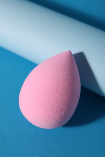 Pink makeup sponge on light blue background, closeup