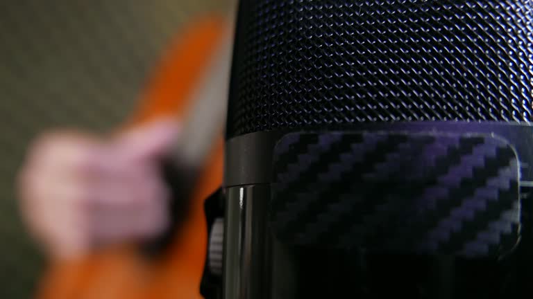 Close-up shot of a microphone in a recording studio: a guitarist strumming an acoustic guitar in a recording studio. USB microphone, front view. Person playing guitar. Man playing an acoustic guitar. Musician playing a musical instrument