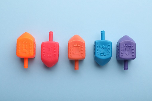 Colorful dreidels on light blue background, flat lay. Traditional Hanukkah game