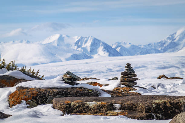 Cairn on a rock with the snow-covered Altai Mountains in the background under a clear sky.