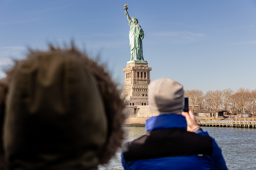 New York City, USA - February 13, 2023 - Tourists taking photos of the Statue of Liberty aboard a ferry from Manhattan to Liberty Island on a winter day