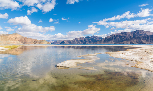 Pangong Tso or Pangong Lake is an endorheic lake spanning eastern Ladakh and West Tibet situated at an elevation of 4.225 m. It is 134 km long and divided into five sublakes, called Pangong Tso, Tso Nyak, Rum Tso (twin lakes) and Nyak Tso. Approximately 50% of the length of the overall lake lies within Tibet in China, 40% in Ladakh, India and the remaining 10% is disputed and is a de facto buffer zone between India and China. The lake is 5 km wide at its broadest point. All together it covers almost 700 km2.\nTwo streams feed the lake from the Indian side, forming marshes and wetlands at the edges. In the sun, the lake is a deep shimmering blue and green backed by barren tan-colored mountains with snows depending on the season, the sight that is stunningly beautiful and pristine. Despite being saline water the lake freezes completely during the winter. The spectacular lakeside is open during the tourist season, from May to September.\nPangong Tso, Ladakh, India, Asia.