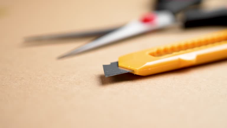 Stationery knife and sharp scissor on brown parcel box cardboard. Office stationery close up. Rotation