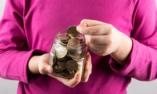 Glass jar with coins of 100 and 200 Kazakhstani tenge in children's hands