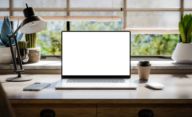 um laptop com uma tela em branco fica em uma elegante mesa de madeira dentro de um interior de estilo loft, com espaços verdes no fundo visíveis através da janela - renderização 3d - warm light - fotografias e filmes do acervo