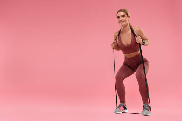 istock Woman exercising with elastic resistance band on pink background, low angle view. Space for text 1954425900