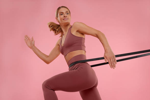 istock Woman exercising with elastic resistance band on pink background, low angle view 1954426482