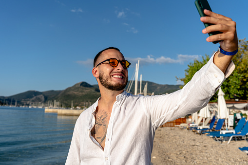 Amidst the soothing sounds of sea waves, a young man pauses to take a perfect selfie, capturing the beach's essence