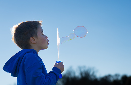 Child blowing soap bubbles with a bubbler with a blue sky in the background