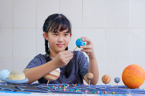 Young Asian girl Making Solar system Model on wooden table at home for her Science Homework project at Elementary school