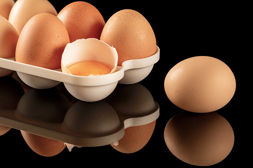 A close-up image of brown chicken eggs displayed on a black mirrored surface. The eggs are reflected in the shiny, reflective background, creating an interesting and captivating visual effect.