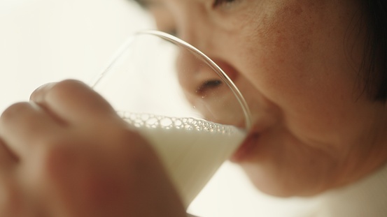 Asian senior woman drinking milk while sitting on sofa at home.