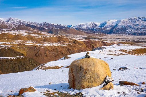 Cairn on a rock with the snow-covered Altai Mountains in the background under a clear sky.