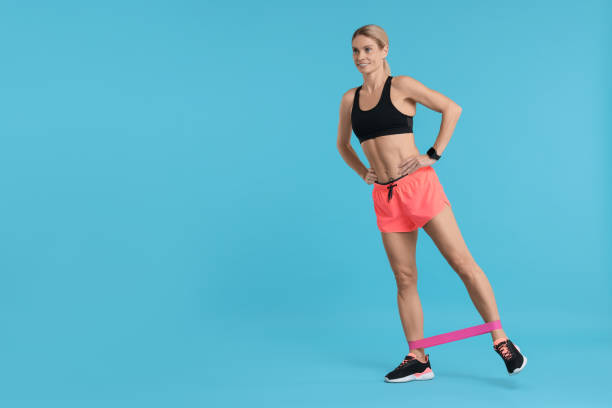 istock Woman exercising with elastic resistance band on light blue background. Space for text 1954456286