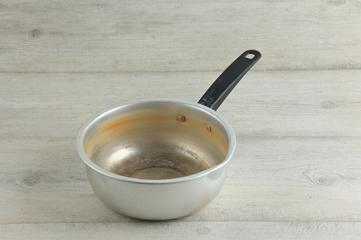 Old Used Stock Noodle Sauce Pan on White Wooden Table, Made from Aluminum with Black Plastic Handle. Isolated