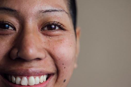 Close up headshot of a young woman standing in front of a cream coloured background. She is looking at the camera while smiling.