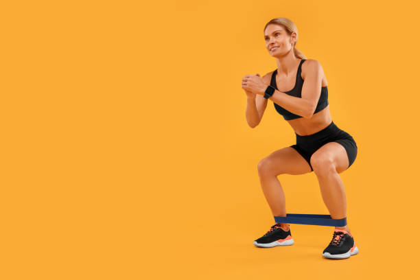 istock Woman exercising with elastic resistance band on orange background, low angle view. Space for text 1954462422