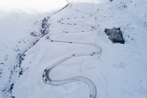 Difficult winter driving conditions on a winding, snow-covered mountain road with cars, Swiss Alps, aerial view.