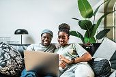 Happy black couple relaxing at cozy sofa with a laptop in living room