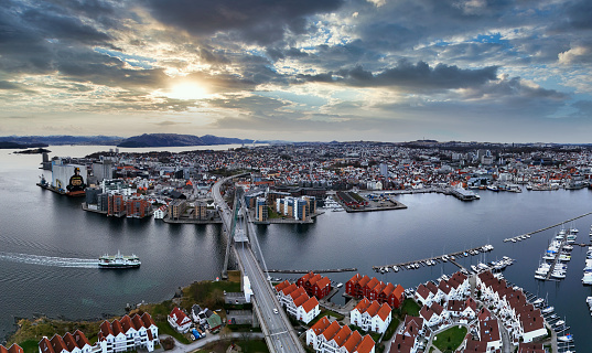 Aerial panoramic view of the city center and harbour bay area with small marinas and a ferry sailing under the iconic Stavanger City Bridge, just before sunset in Stavanger, Norway