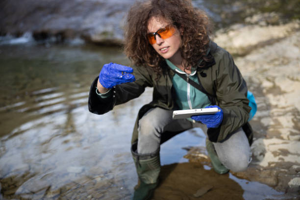 Mid Adult Caucasian Female Environment Researcher Checking Mechanical and Biological Possible Pollution Causes of Water Stream on the Field Outdoors and Collecting Impressions data on a Digital tablet investigadora del medio ambiente de la mujer caucásica adulta media comprobación de las posibles causas de contaminación mecánica y biológica de la corriente de agua en el campo al aire libre y recopilación de datos de impresiones en una tableta digi