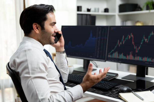 istock Trader calling to consultant or partner with two stock exchange screen. Surmise. 1954516495