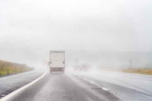 A driver's point of view on a motorway journey during heavy rainfall, with poor visibility of traffic in the distance.