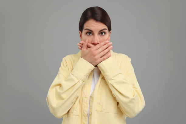 istock Embarrassed woman covering mouth with hands on grey background 1954542974