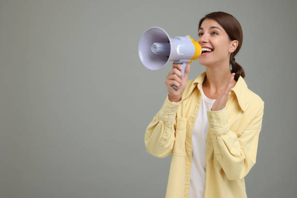istock Special promotion. Young woman shouting in megaphone on grey background, space for text 1954547273