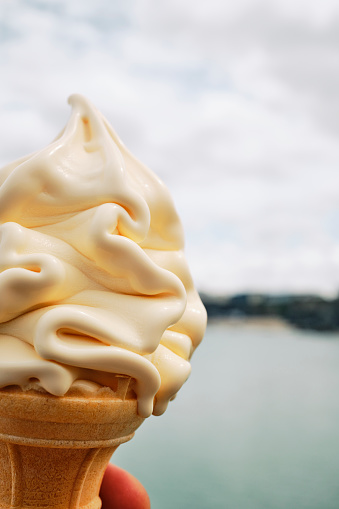 POV of a vanilla soft Ice Cream cone at the coast in Newquay, Cornwall, UK on a June day.