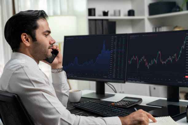 istock Trader calling to consultant or partner with two stock exchange screen. Surmise. 1954574349