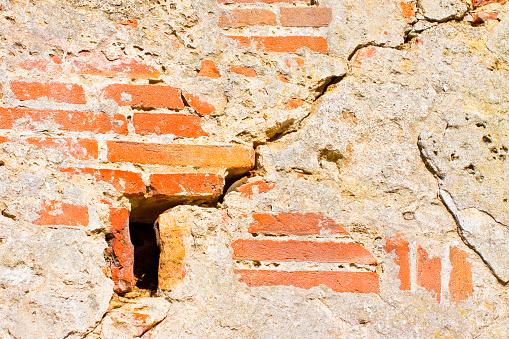 Deep crack in old brick and stone wall with damaged plaster