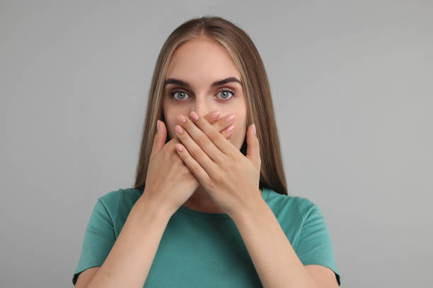 istock Embarrassed woman covering mouth with hands on grey background 1954592473