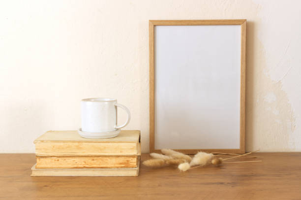 istock Horizontal white frame mockup on a vintage wooden bench, table, ceramic mug, and saucer with dry Lagurus ovatus grass. White wall background. Scandinavian interior. Selective focus. 1954607777