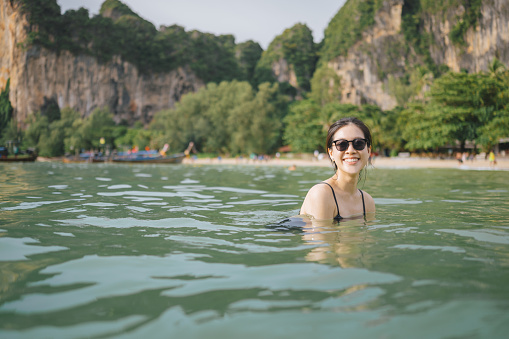 POV asian woman relaxing in the water with sunglasses ,Portrait of happy cheerful woman in bikini floating in tropical paradise Beachfront Swimming Pool