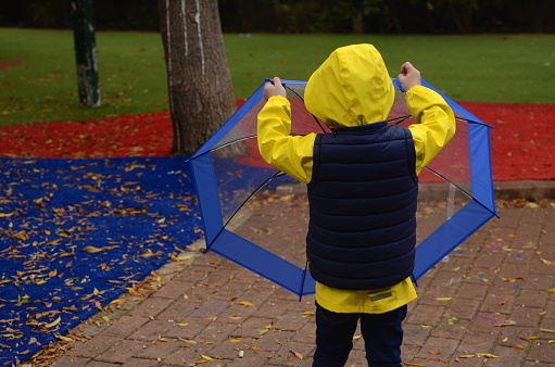 Portrait of a child in the rain. Boy 3 years old in a yellow raincoat and hood, laughs and smiles. Walking in the rain, waterproofs