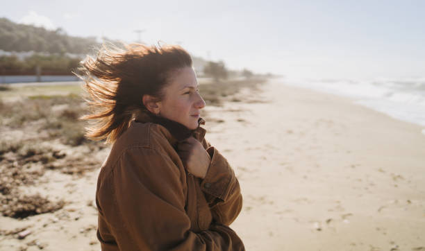 Smiling woman with tousled messy long blond hair against clear blue sky at beach. Portrait of happy beautiful female enjoying during summer vacation.