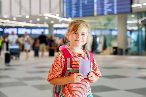 Little preschool girl at airport terminal. Happy child going on vacations by airplane. Smiling kid with passport and bag